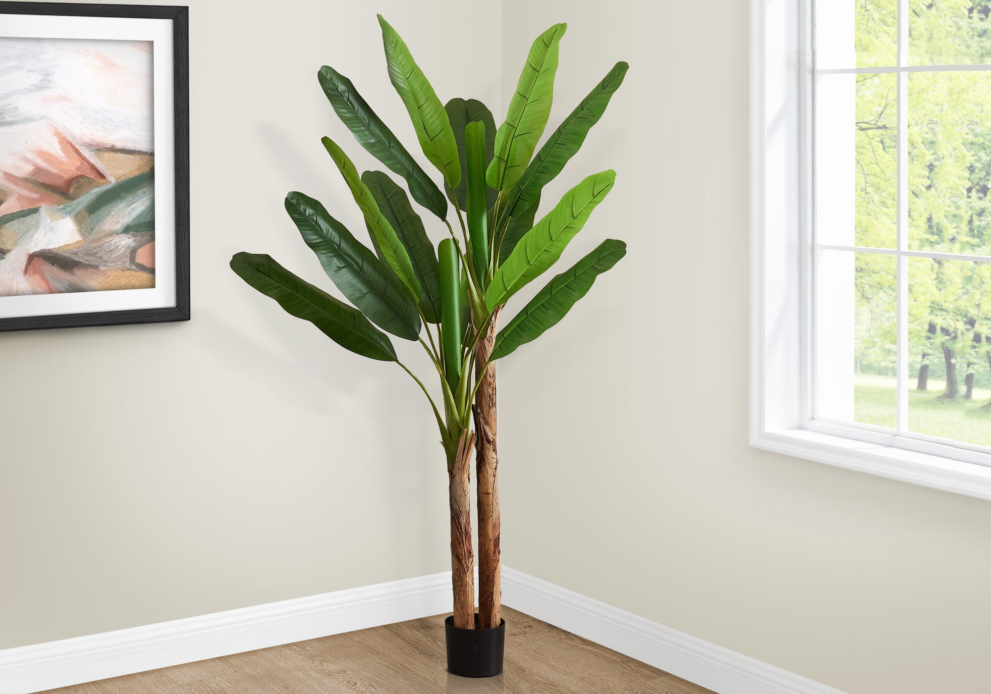 A tall artificial banana plant with large green leaves stands in the corner of a room next to a window.