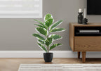 A medium artificial variegated rubber tree in a black pot sits on a wooden floor beside a wooden media console.