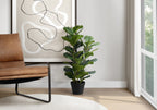 Artificial fiddle leaf fig bush in a black pot placed next to a brown leather chair and abstract wall art.