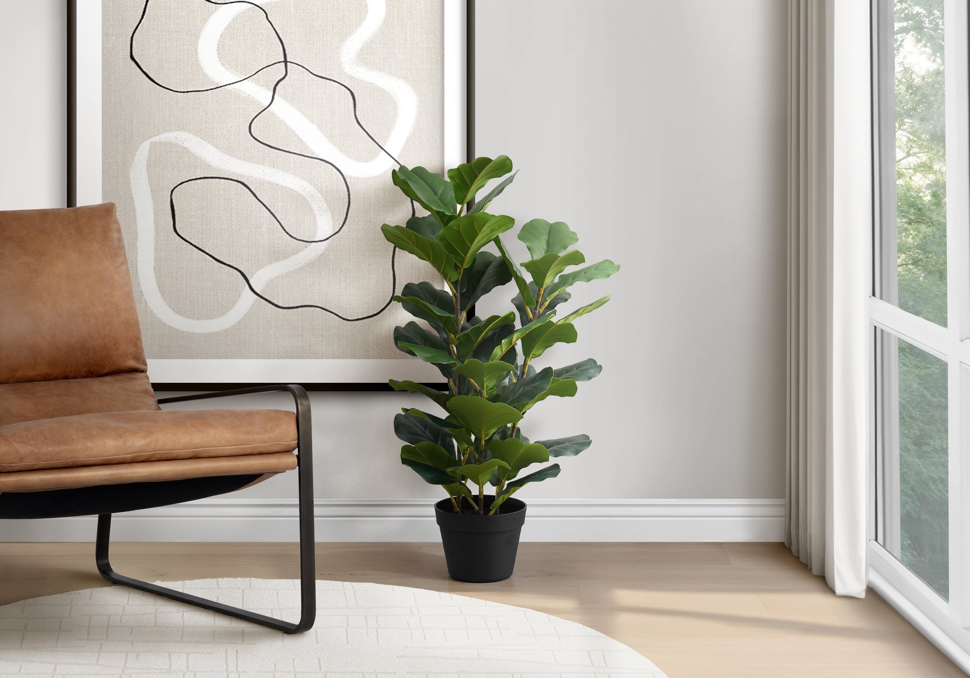 Artificial fiddle leaf fig bush in a black pot placed next to a brown leather chair and abstract wall art.