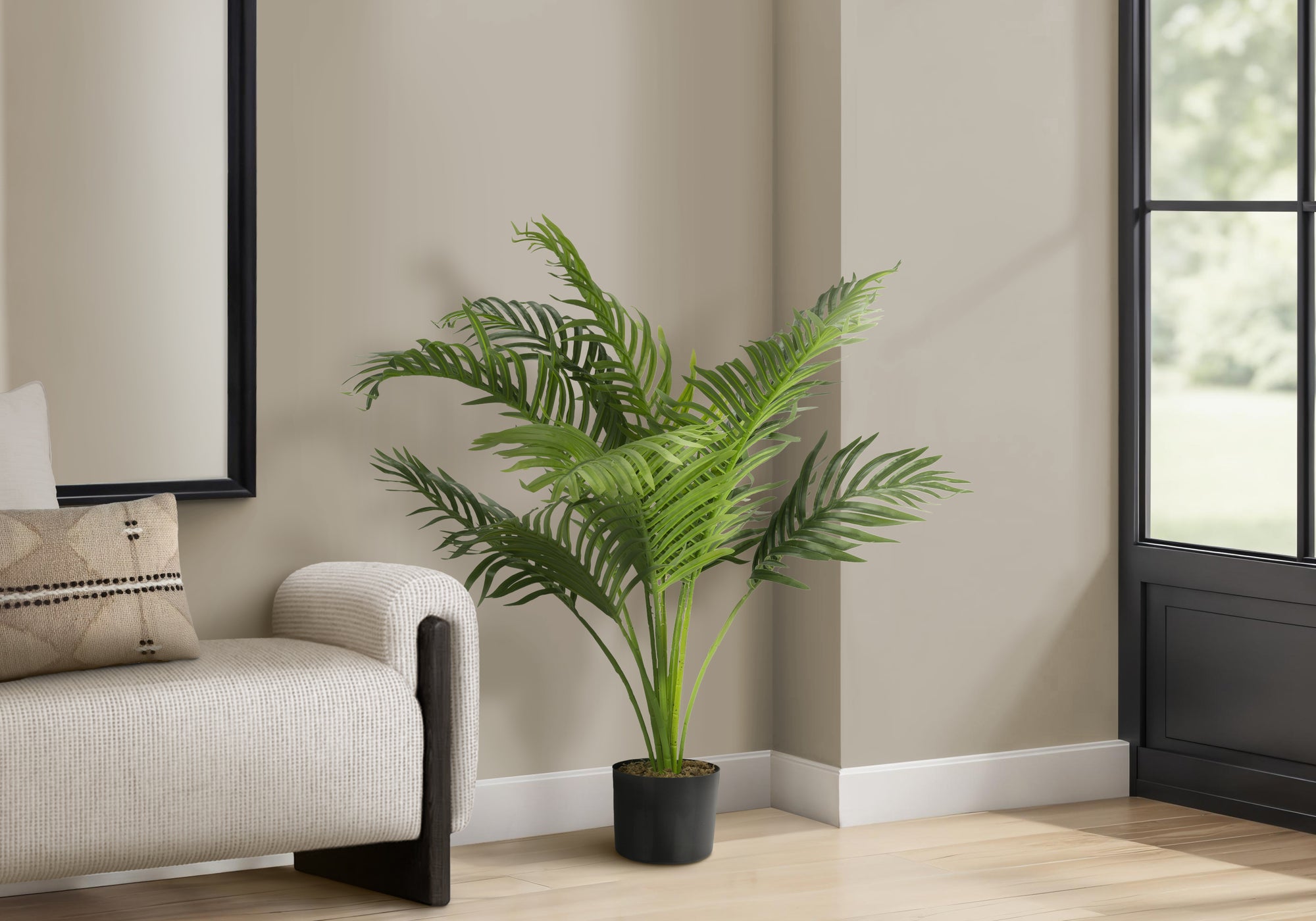An artificial Cat Palm with wide, green fronds in a black pot, placed in a corner next to a modern armchair.