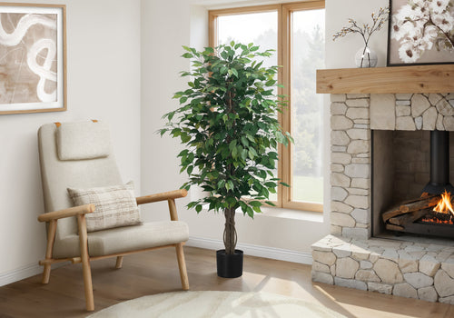 A tall artificial ficus tree in a black pot stands in a cozy living room next to a cream armchair and stone fireplace.