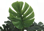 Close-up of a large green split leaf on an artificial Monstera plant against a white background.