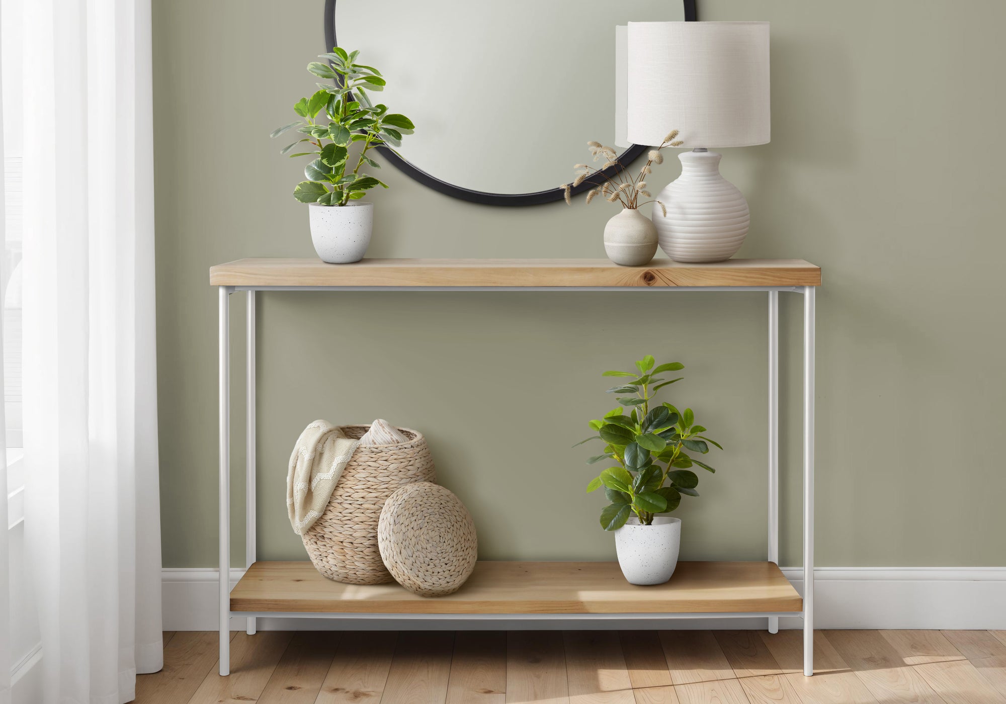 Two artificial baby rubber plants in speckled white pots styled on a wooden console table with a lamp and basket.