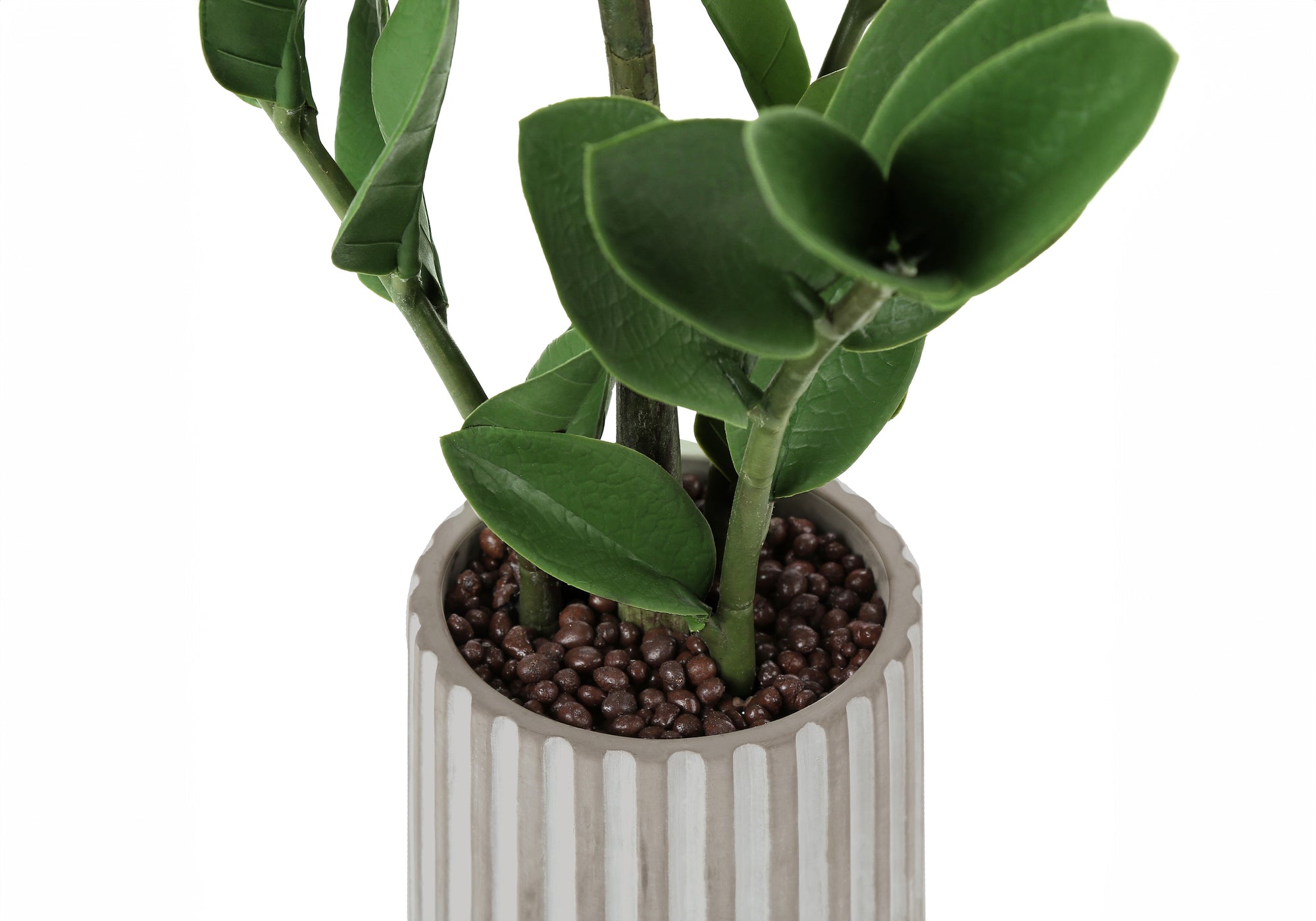 An artificial small ZZ plant in a ribbed grey pot filled with brown pebbles, shown in a close-up view.