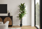 A tall artificial Dracaena tree with layered trunks and long green leaves standing in a modern living room corner.