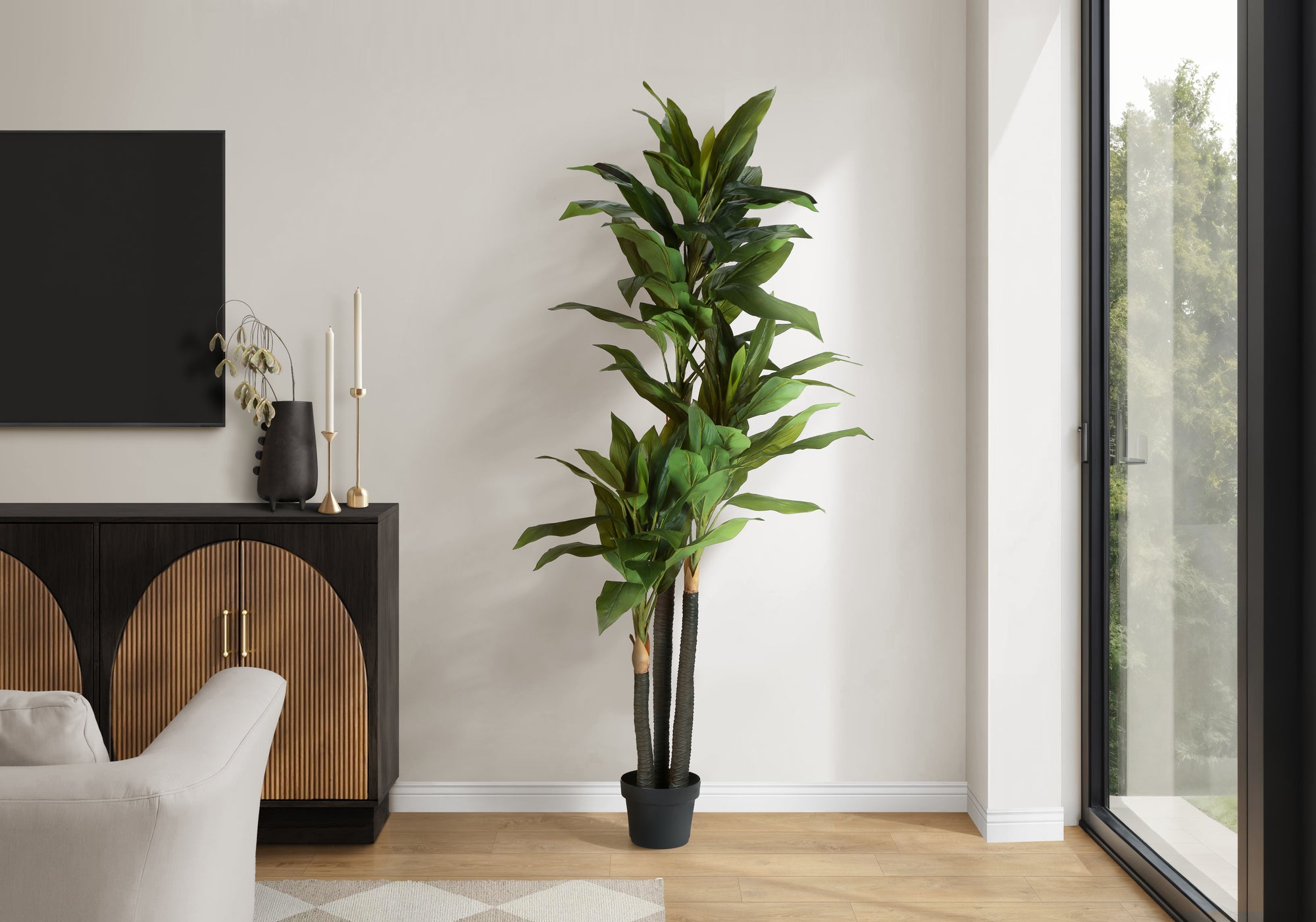 A tall artificial Dracaena tree with layered trunks and long green leaves standing in a modern living room corner.