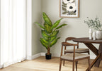 A tall artificial Dieffenbachia plant with variegated green leaves stands in the corner of a bright dining room.