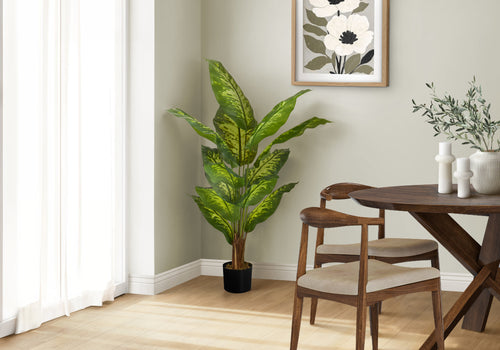 A tall artificial Dieffenbachia plant with variegated green leaves stands in the corner of a bright dining room.