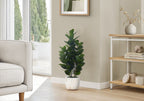 A medium-sized artificial Garcinia bush with dense, dark green leaves in a white marbled pot, placed in a living room.