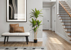A tall faux Dracaena tree with three trunks stands in a bright entryway next to a white bench with leather pillows.