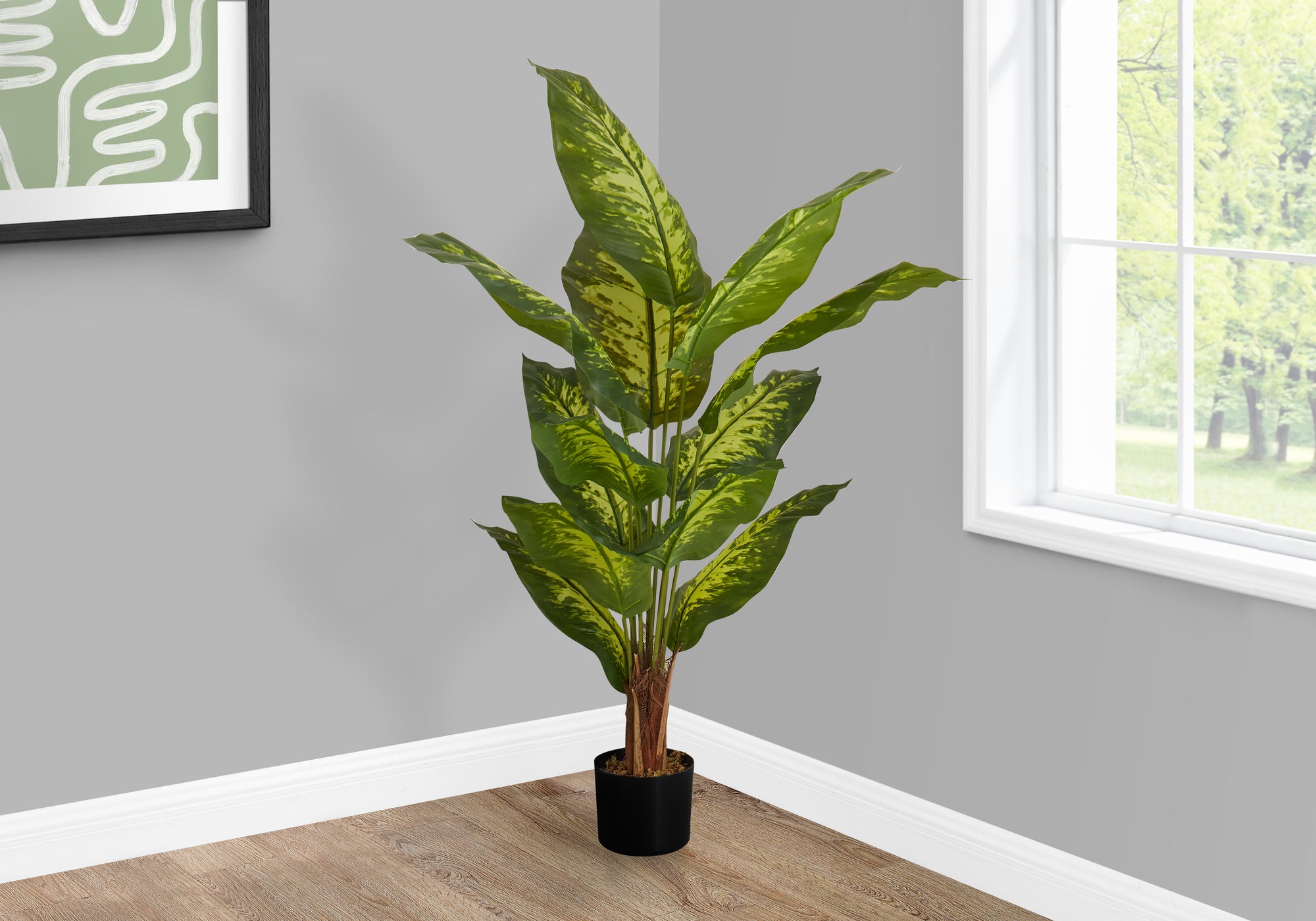 A tall artificial Dieffenbachia plant with large, variegated green leaves in a black pot, placed in a room corner.