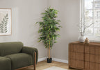 A tall artificial bamboo tree in a black pot standing in the corner of a living room next to a green sofa.