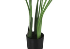 Close-up of the base and green stems of an artificial Bird of Paradise plant in a simple black plastic pot.