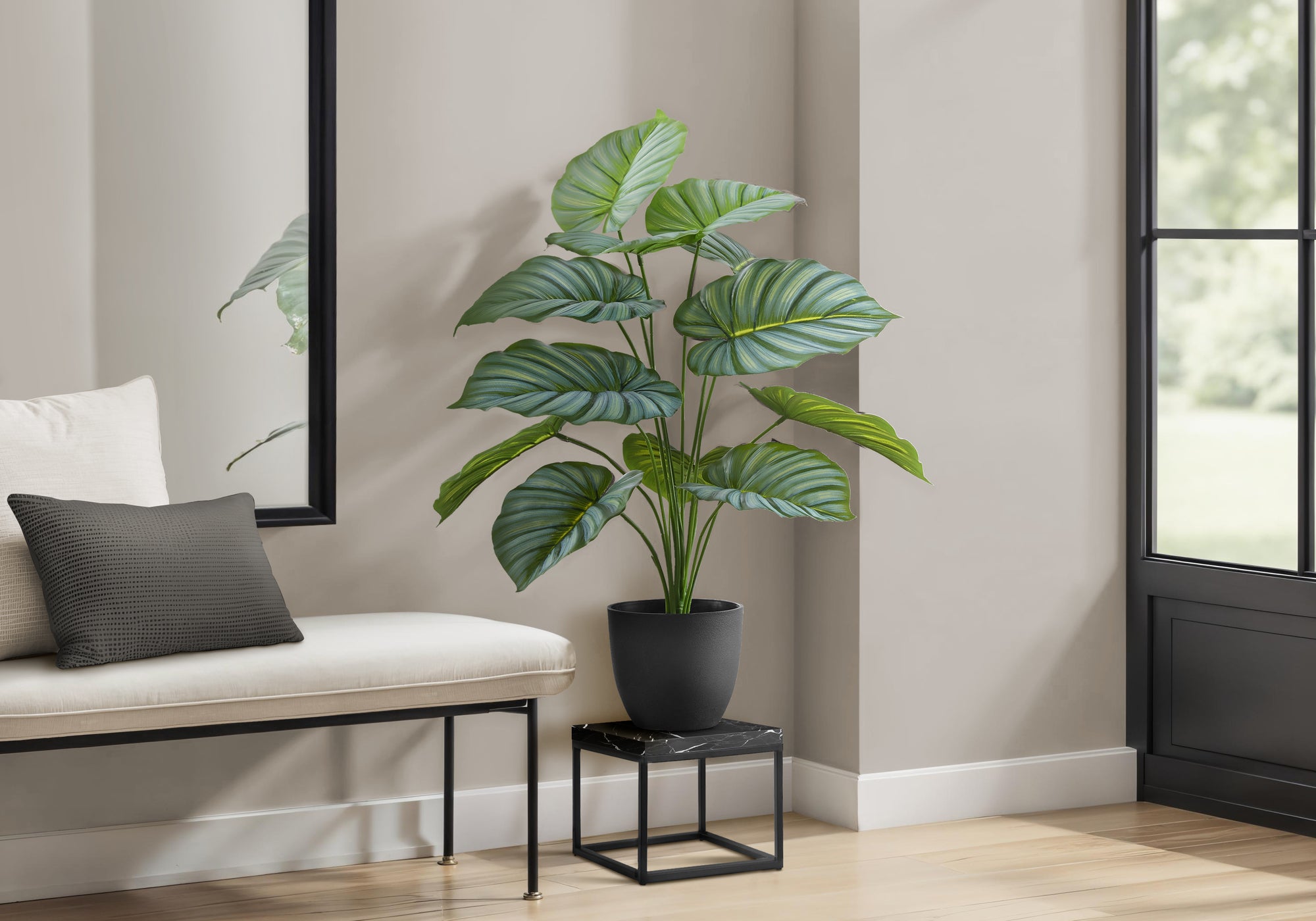 A faux Calathea Orbifolia plant with large striped leaves in a black pot, sitting on a small marble-topped stand.