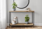 Two artificial baby rubber plants in grey pots styled on a wooden console table with white vases and a round mirror.