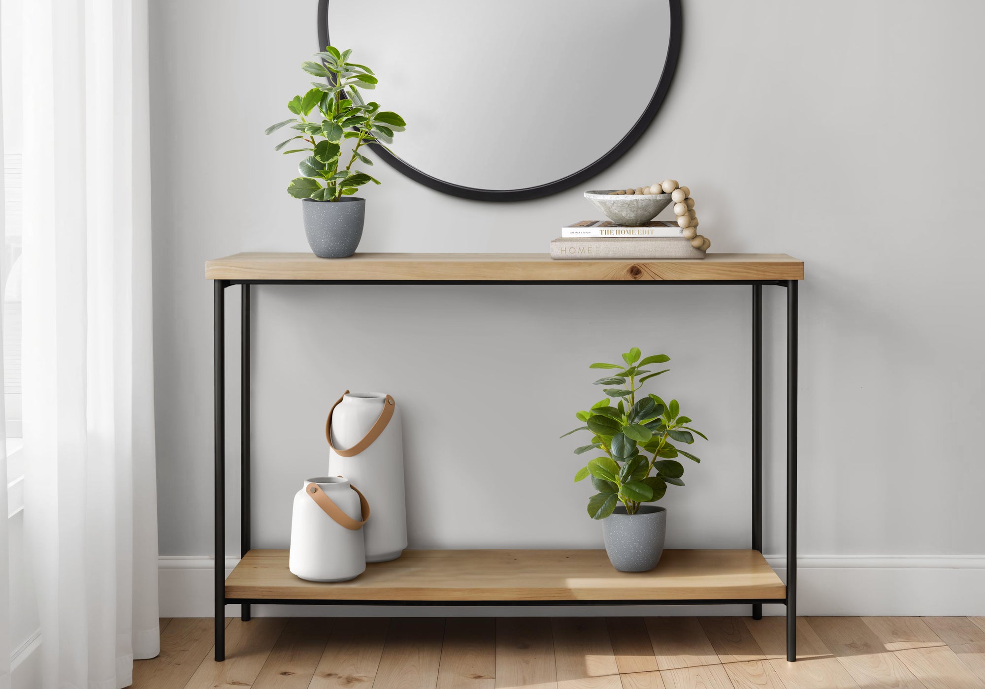 Two artificial baby rubber plants in grey pots styled on a wooden console table with white vases and a round mirror.