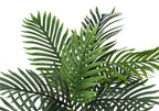 Close-up of the lush green fronds of an artificial parlor palm plant against a white background.
