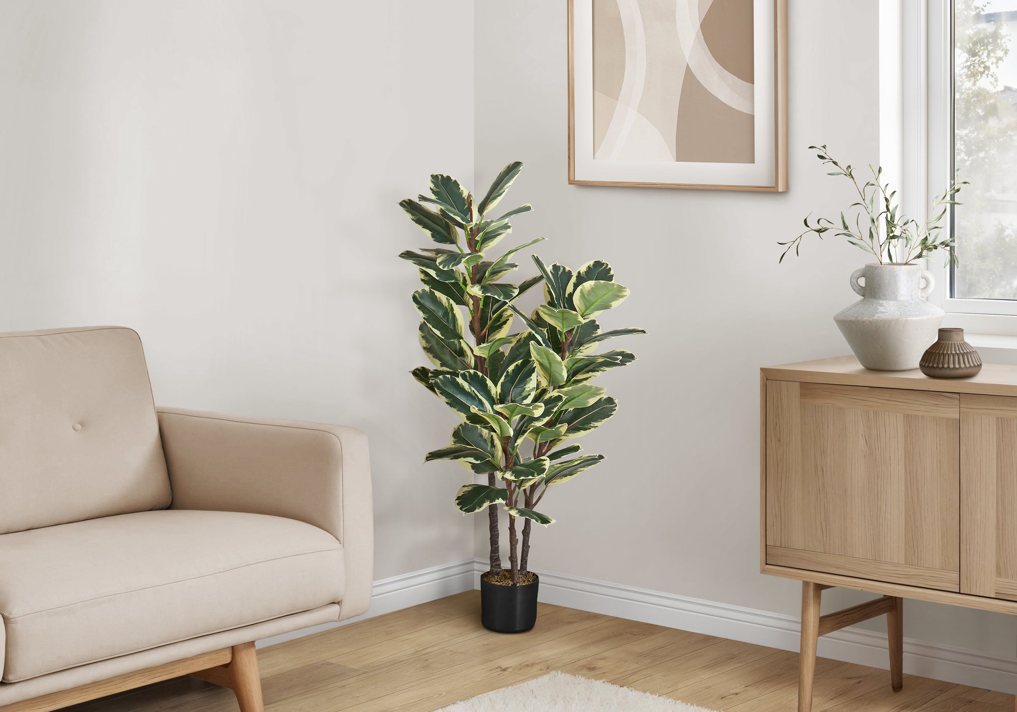 A large artificial variegated rubber plant in a black pot stands in the corner of a bright, modern living room.