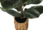 Close-up of an artificial fiddle leaf fig plant in a woven boho basket with black faux soil.
