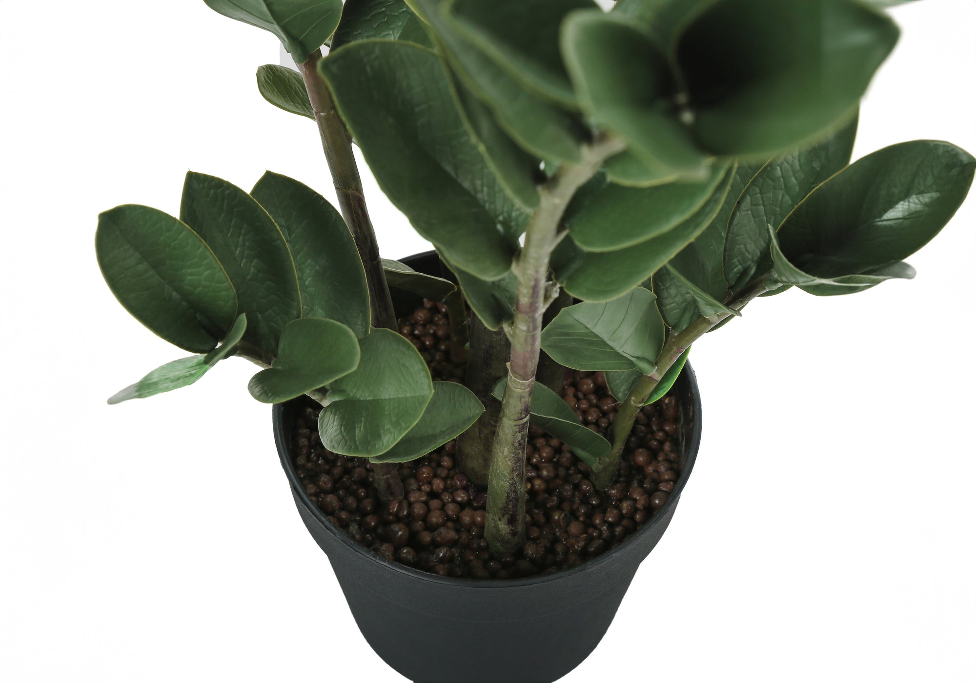 Top-down view of an artificial ZZ plant with dark green, structured leaves in a simple black pot with brown soil.