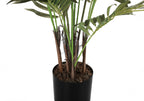 Close-up of the base of a faux Areca palm tree showing textured brown trunks and green fronds in a black pot.