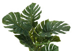 Close-up of a large artificial Monstera plant with deep green, split-leaf foliage against a white background.