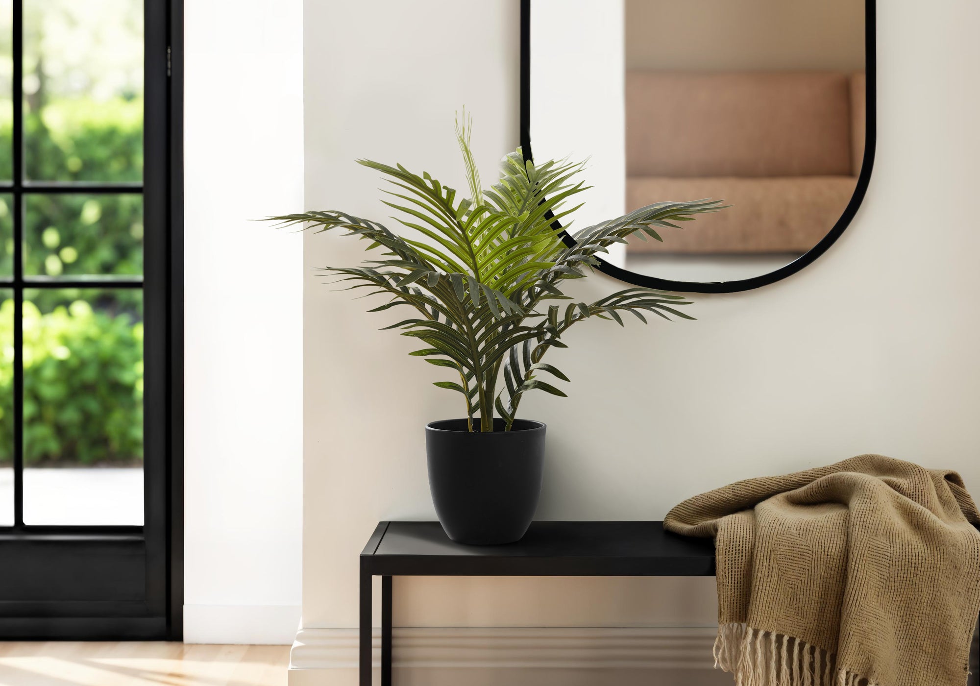 Artificial Medium Areca Palm in a black pot on a black console table next to a beige throw blanket.