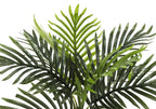 Close-up of the lush green fronds of an artificial areca palm plant against a white background.