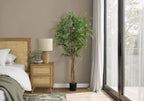 A tall artificial weeping fig tree with a braided trunk stands in a modern bedroom next to a rattan nightstand.