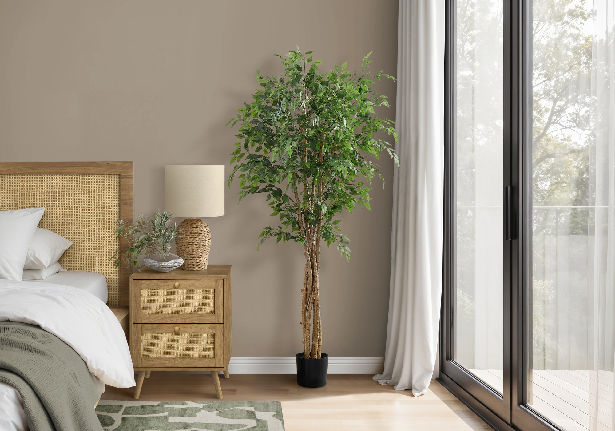 A tall artificial weeping fig tree with a braided trunk stands in a modern bedroom next to a rattan nightstand.