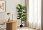 Tall artificial Monstera tree with split leaves and dual trunks standing in a corner next to a wooden desk.