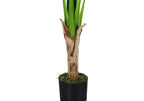 Close-up of the textured trunk and green stems of an artificial banana tree in a black pot with moss.