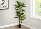 A tall artificial Monstera tree with dual trunks and split leaves standing in the corner of a bright room.