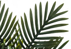 Close-up of the green fronds of an artificial areca palm plant against a plain white background.