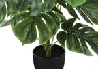 Close-up of a faux Monstera plant showing split green leaves, stems, and black nursery pot