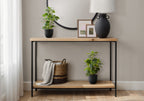 Two artificial baby rubber plants in black pots styled on a wooden console table with a basket and decor items.