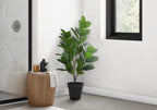 Artificial Medium Garcinia Tree in a black pot styled in a bright room corner next to a wooden stool.