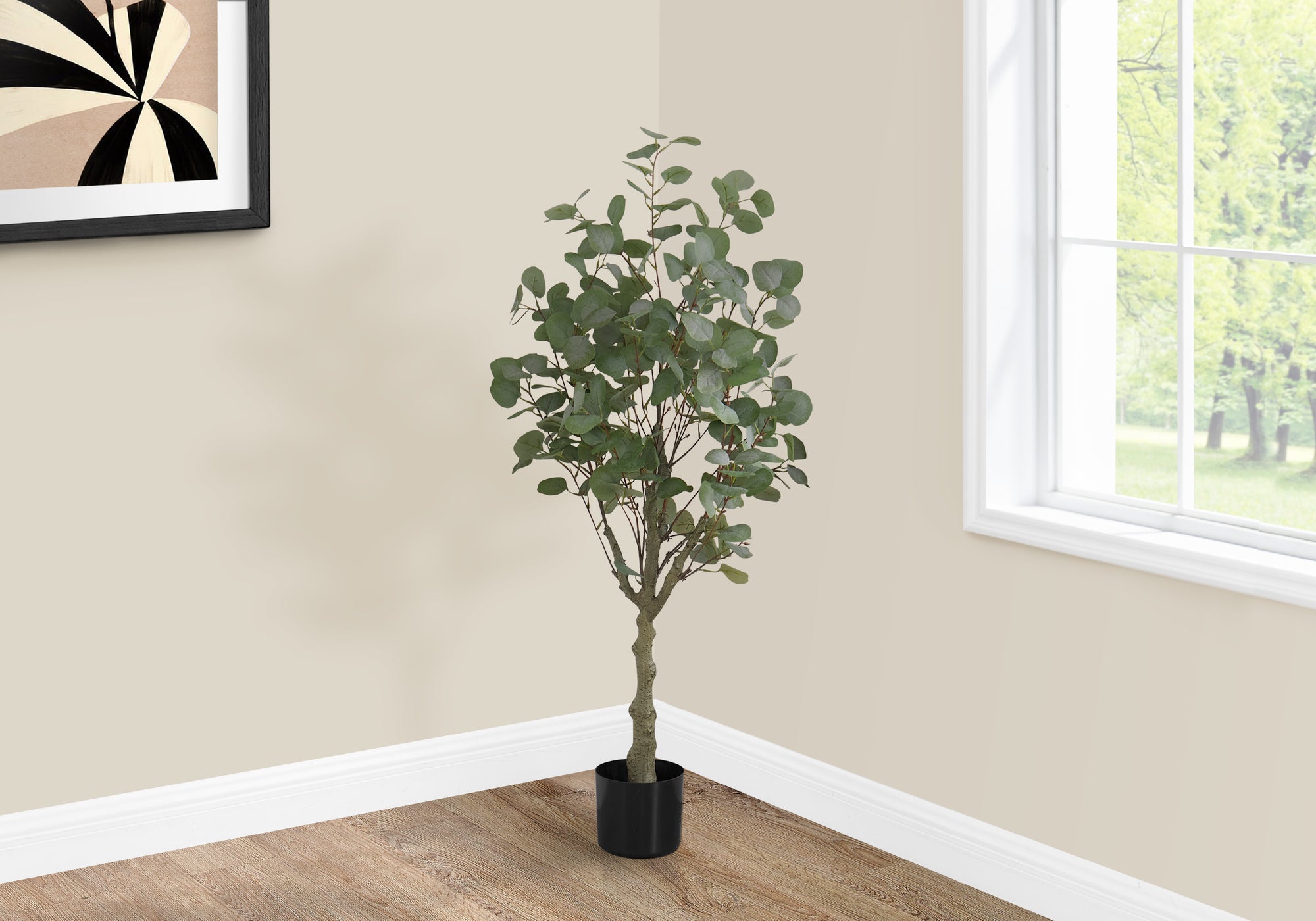 A tall artificial eucalyptus tree in a black pot stands in the corner of a room near a window and framed wall art.