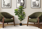 Artificial fiddle leaf fig bush in a black pot centered between two olive green armchairs against a neutral wall.