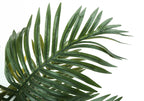 Close-up of a long, green artificial palm leaf with slender, pointed leaflets against a white background.