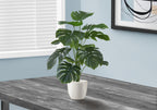 Artificial medium Monstera plant with split green leaves in a white pot, sitting on a dark wooden table.