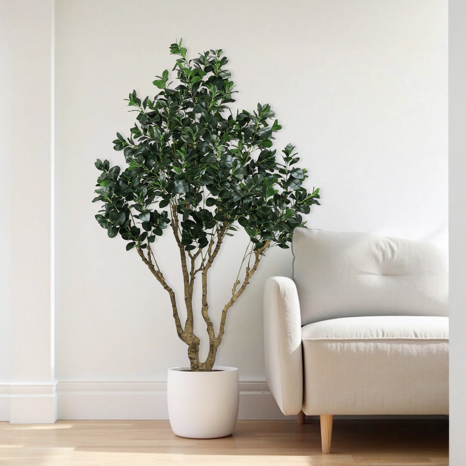 A tall artificial Ficus Moclame tree in a white pot next to a light-colored armchair.