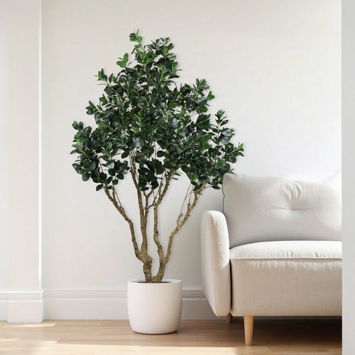 A tall artificial Ficus Moclame tree in a white pot next to a light-colored armchair.