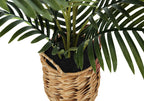 Close-up of an artificial parlor palm's green stems and fronds in a woven basket with dark faux soil.