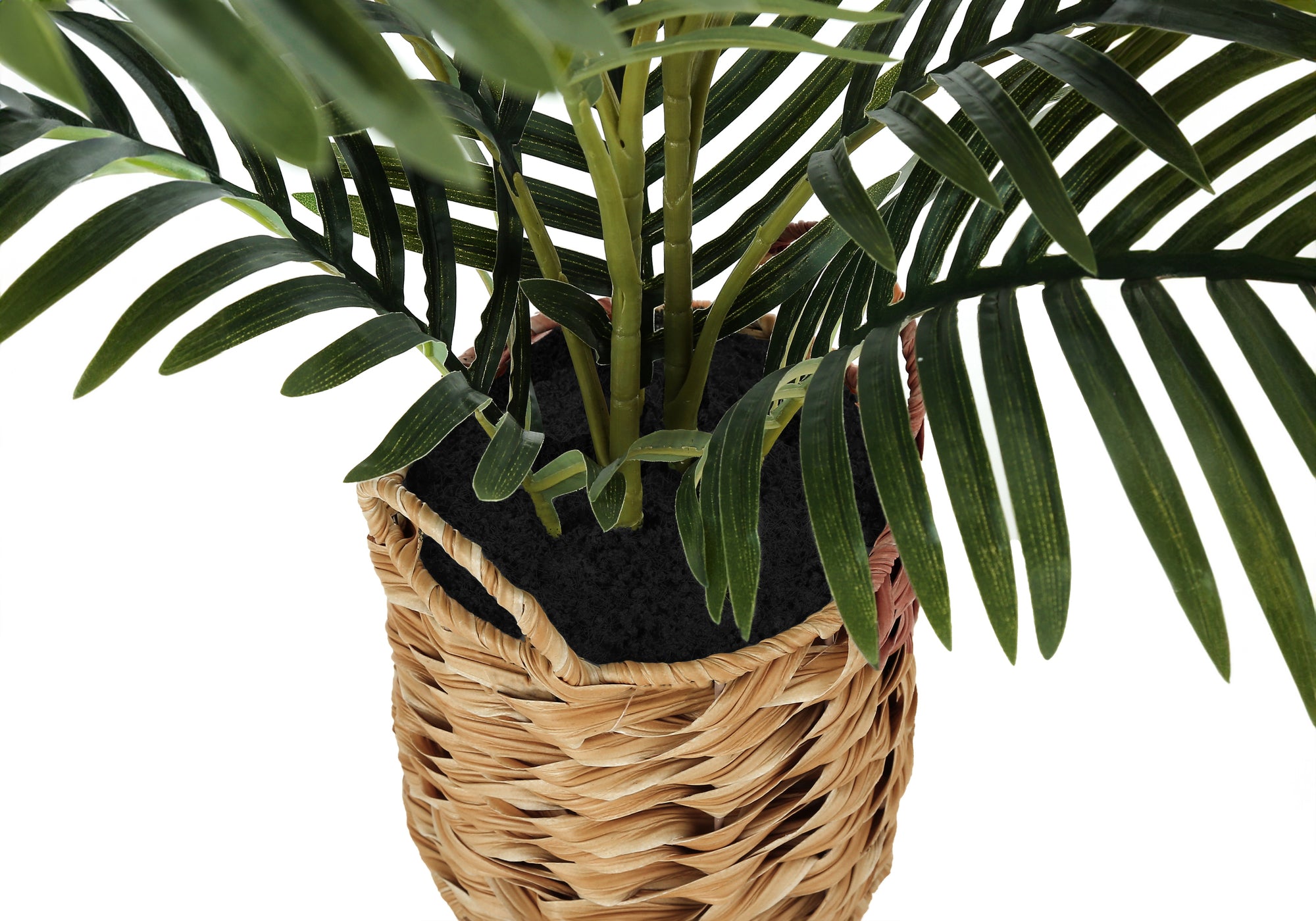 Close-up of an artificial parlor palm's green stems and fronds in a woven basket with dark faux soil.